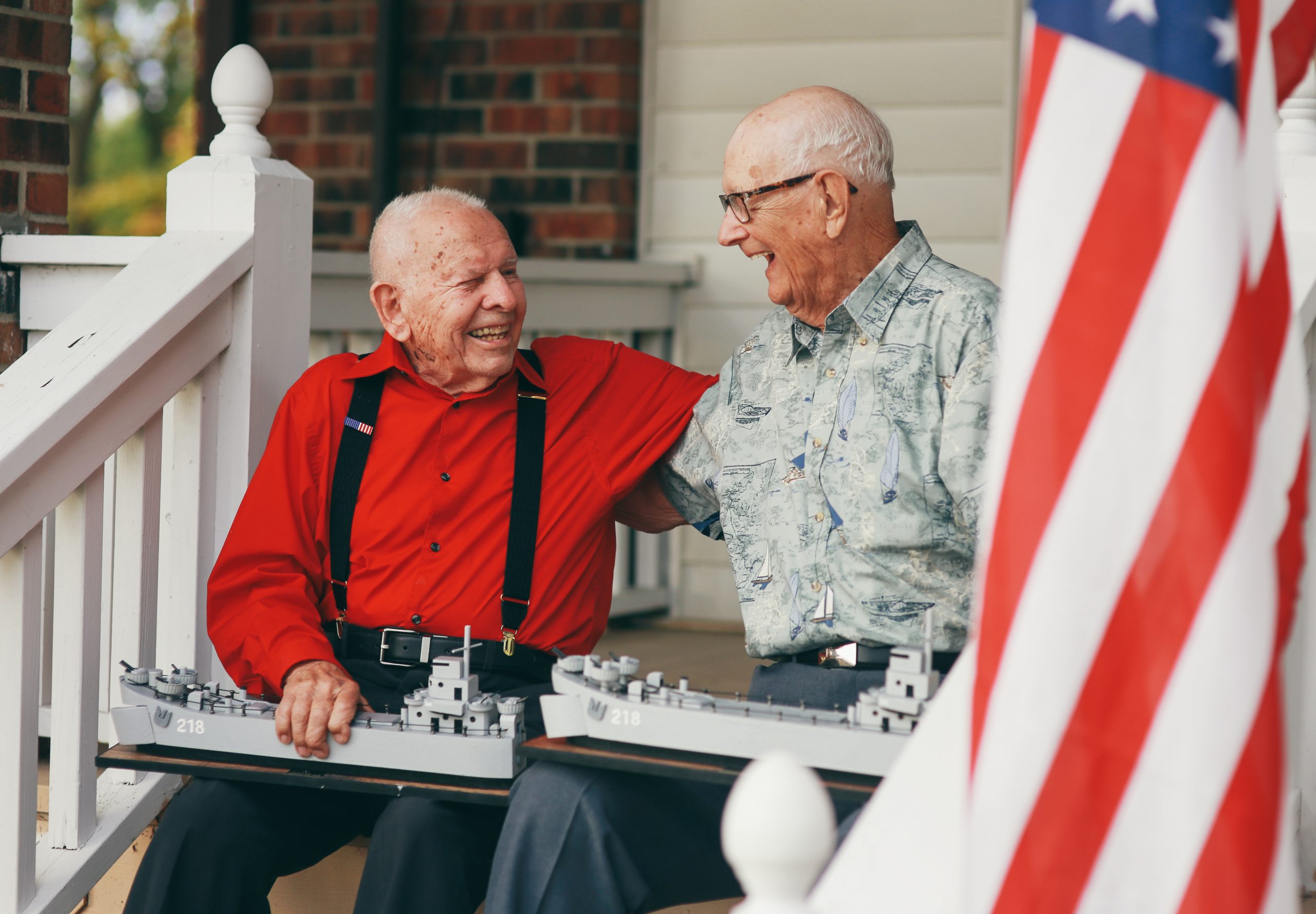 John and DeVere from the movie, The Last Signal, are sitting together embracing on the front porch, holding scaled models of the Navy ship they were on together.