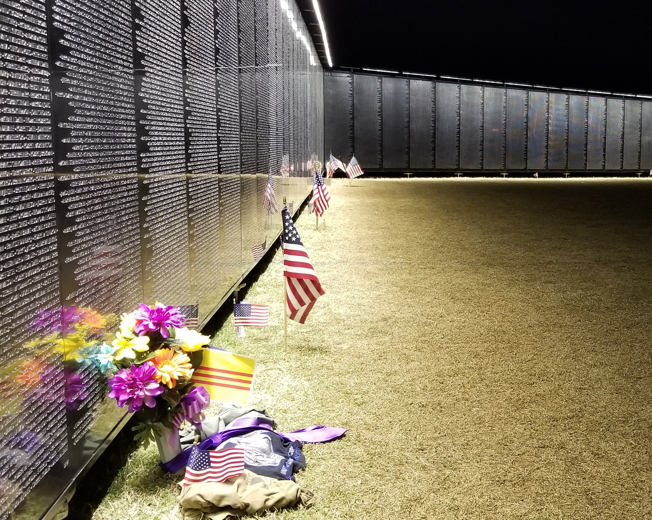 The Wall That Heals at night with flags and flowers left at the base of the Vietnam Veterans Memorial Replica